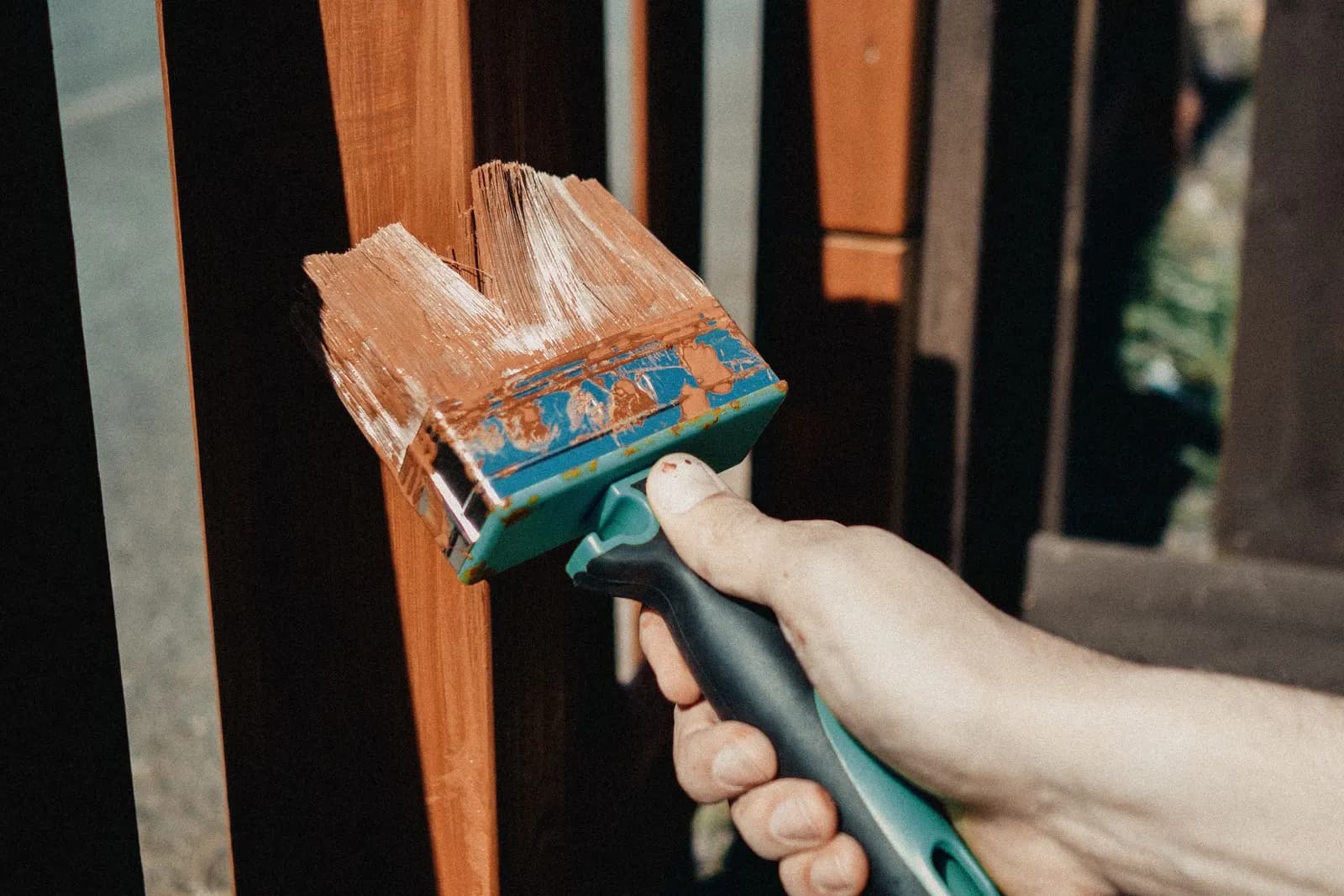 A hand staining a wooden fence with a wide brush