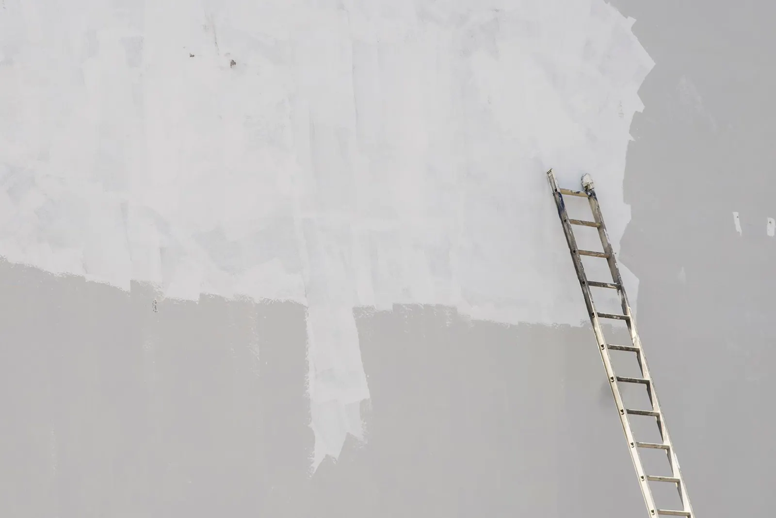 An extension ladder leaning against a tall outside wall with a fresh patch of white paint